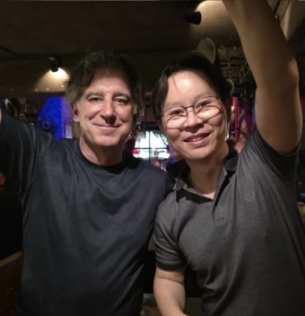 Two people taking a selfie in a dimly lit indoor setting, smiling at the camera.