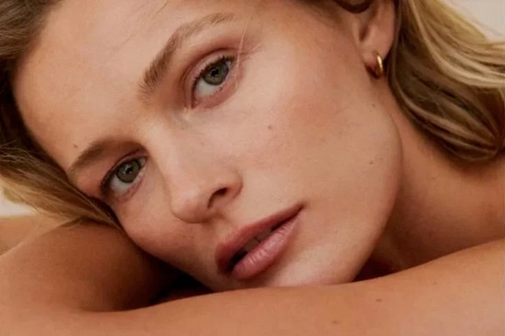 Close-up of a young woman with blonde hair, blue eyes, and light skin resting her face on her arm.