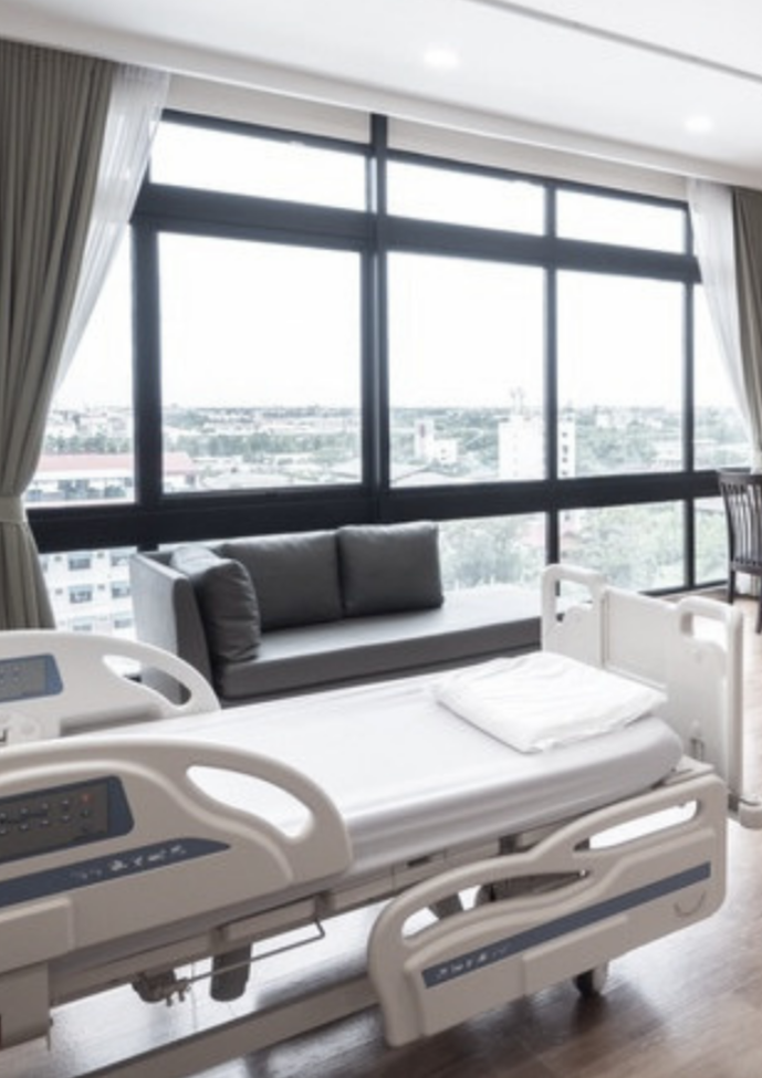 A hospital room with a hospital bed, a pillow, and large windows with city view.