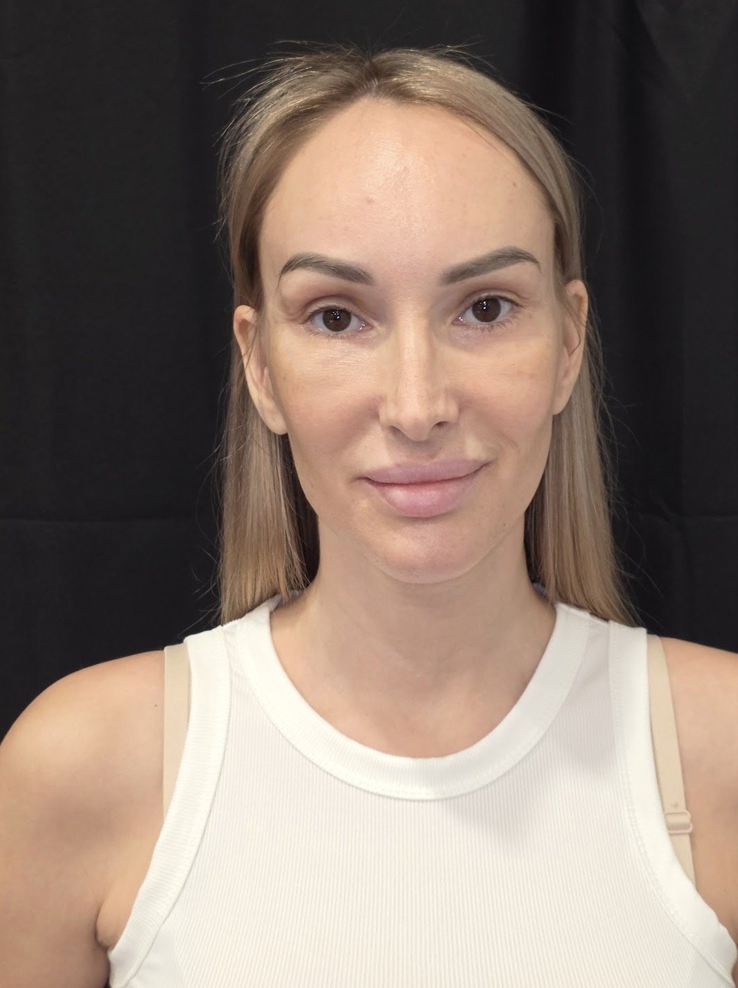 Portrait of a woman with blonde hair wearing a white tank top, smiling softly against a black background.