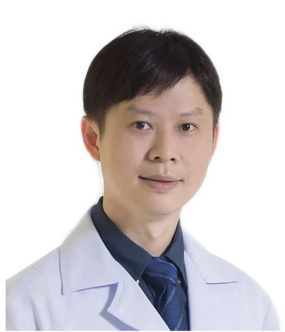 A man wearing a white lab coat, blue shirt, and tie, posing against a plain white background.