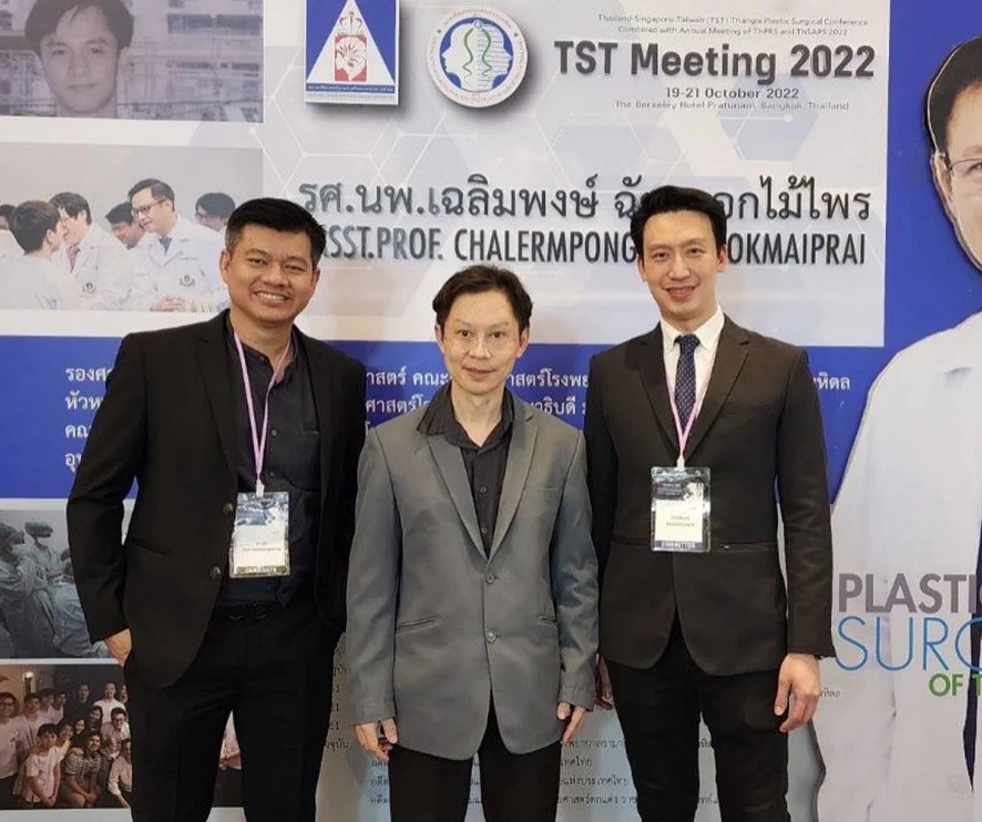 Three men in formal suits standing in front of a conference banner, smiling for a photo at the TST Meeting 2022, October 19-21, in Thailand.