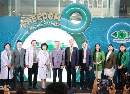 Group of eleven people standing on stage at an event with a blue backdrop, some holding microphones or awards, and a person in the foreground taking a picture.