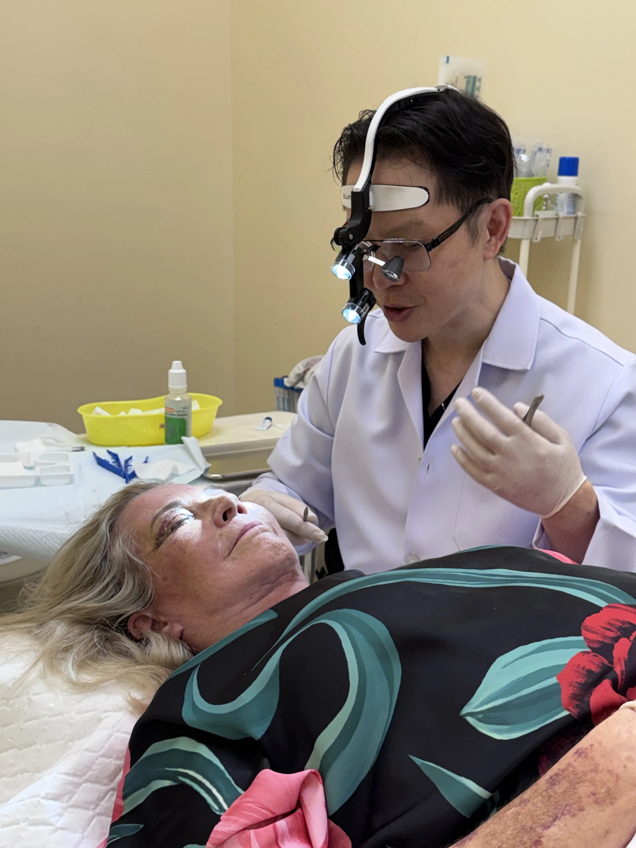 Medical professional performing a procedure on an elderly woman lying on a bed, with various medical supplies visible in the background.