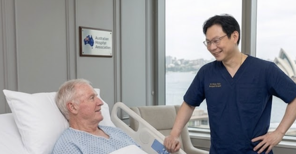 A nurse smiling and talking to an elderly male patient in a hospital room with a view of water and city buildings outside the window