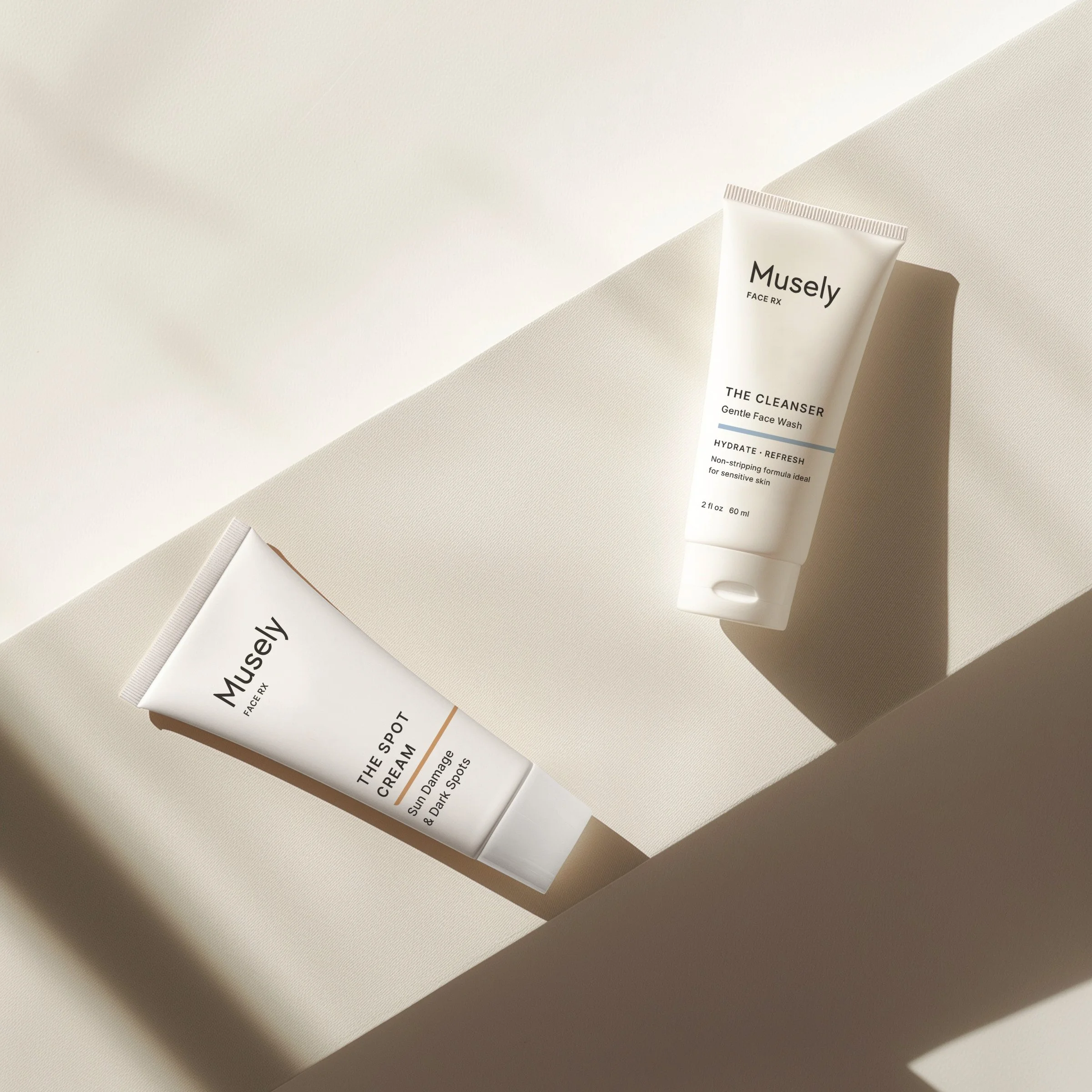 Two white skincare product tubes from Musely, one labeled 'The Spot Cream for dark spots,' and the other 'The Cleanser Gentle Face Wash,' placed on geometric white platforms with shadows.