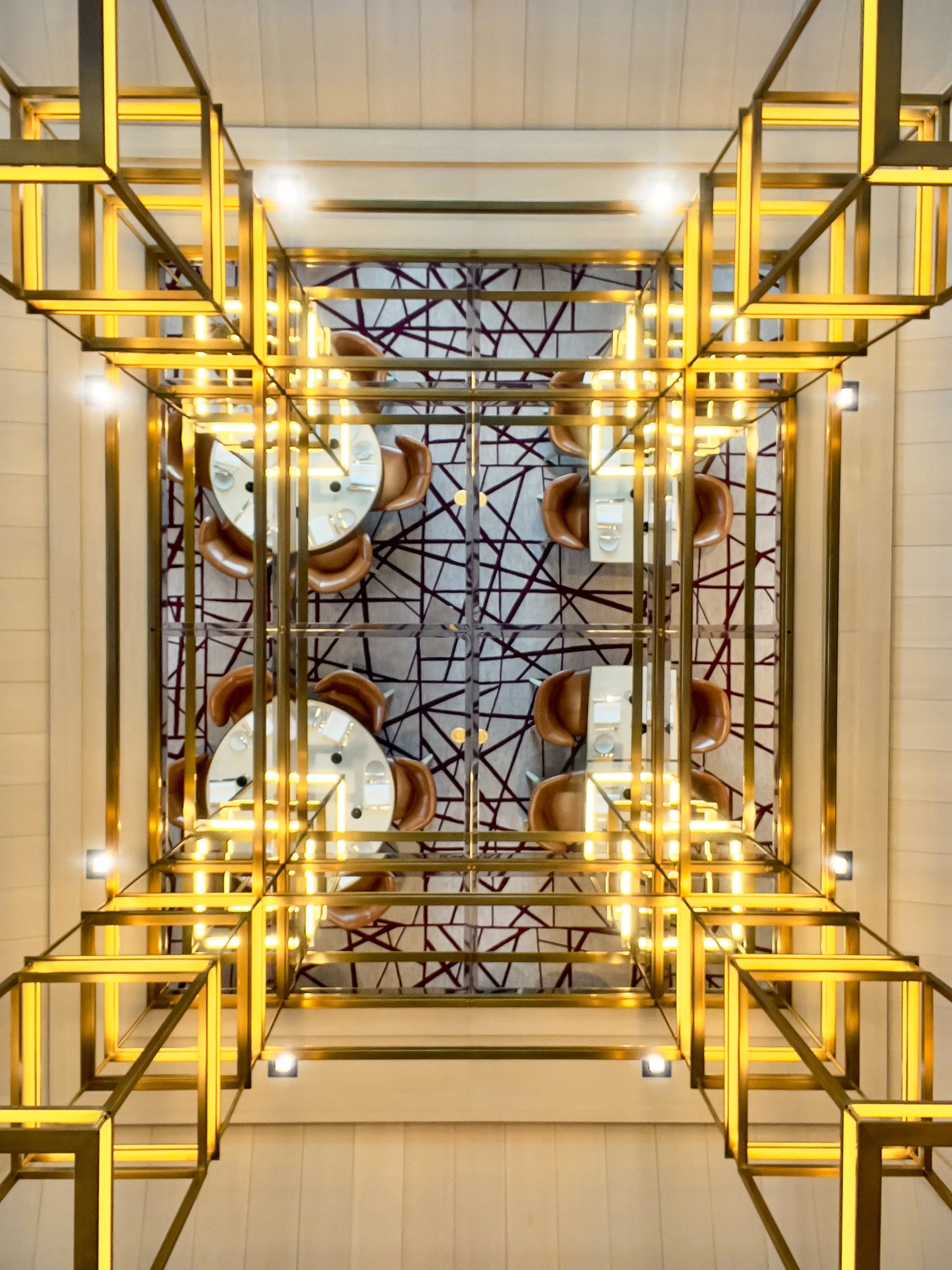 A view looking down from a staircase with a decorative lighting fixture and chairs around a table at the bottom.