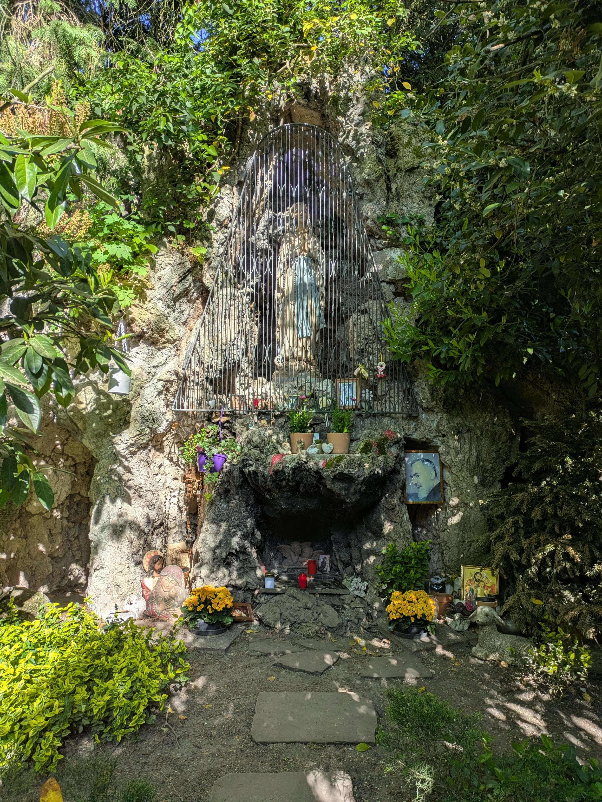 Ein Beton-Felsen, in dessen Felsspalte eine Figur der Mutter Gottes steht. Davor ist ein Gitter. Der Felsen ist geschmückt mit Blumen und Bildern.