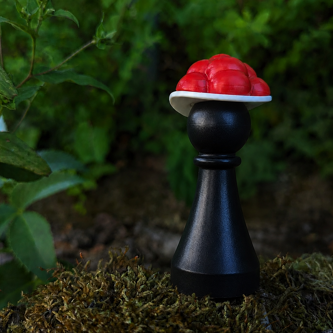 Eine schwarze Spielfigur mit einem Hut, auf dem rote Kugeln liegen.
