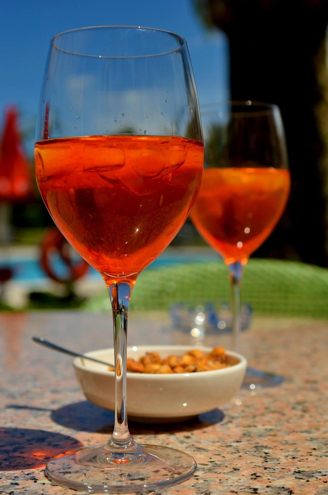 Mit orangenem Aperol gefüllte Gläser stehen auf einem Tisch. Der Himmel dahinter ist blau.