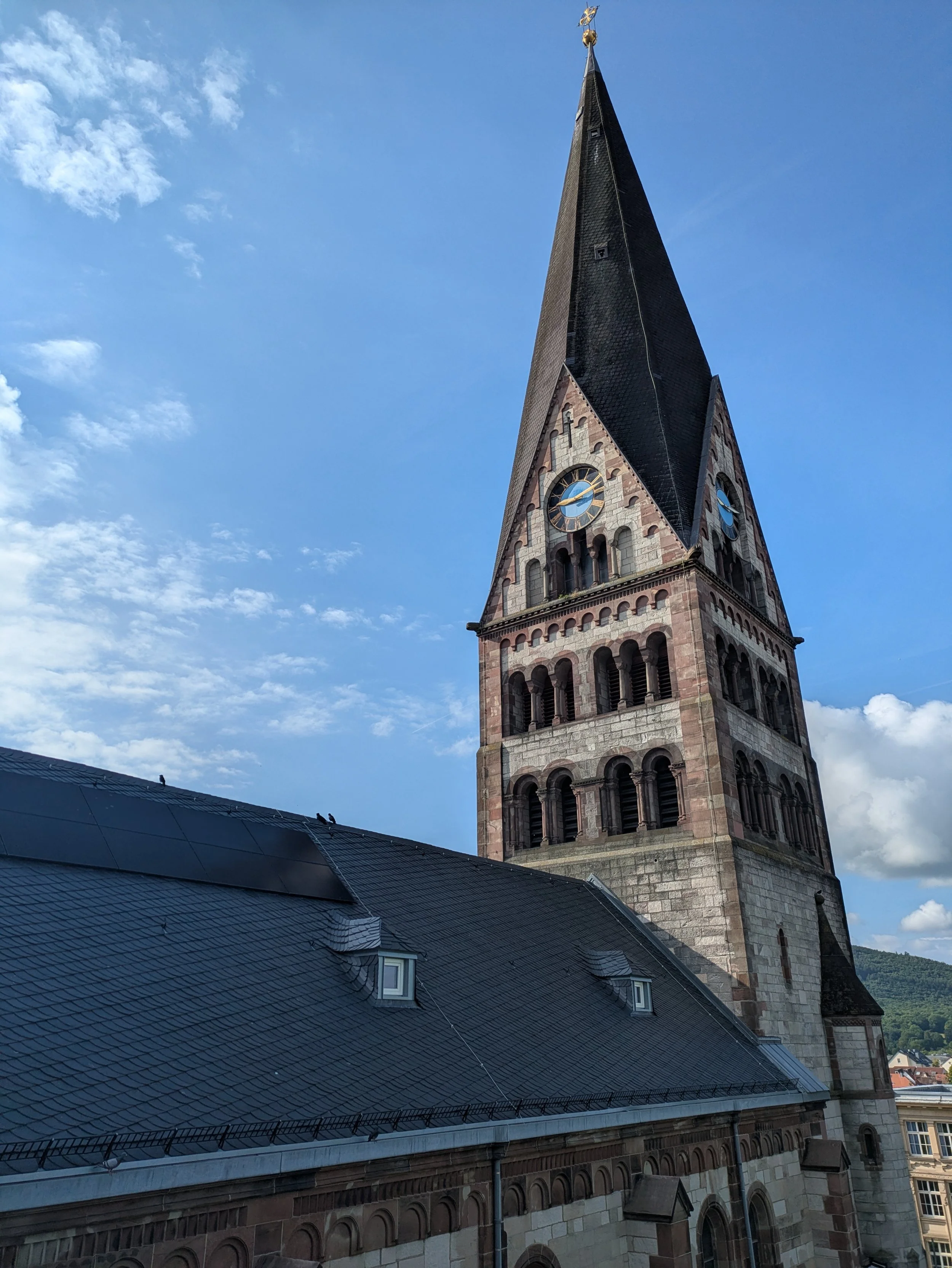 Ein Kirchturm und das Dach einer Kirche, auf dem eine PV-Anlage installiert worden ist,