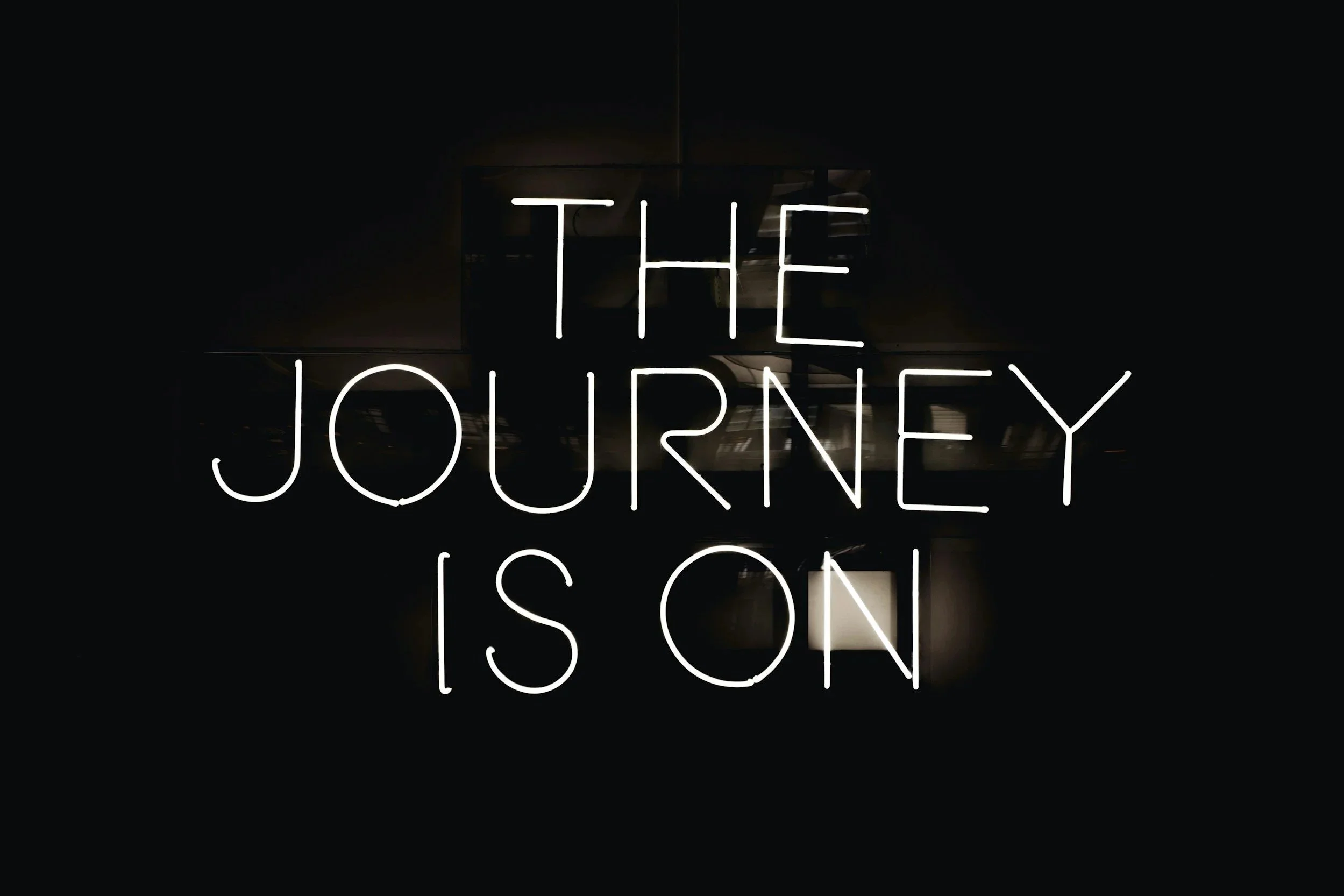 Neon sign with the words 'THE JOURNEY' in white, illuminated against a dark background.