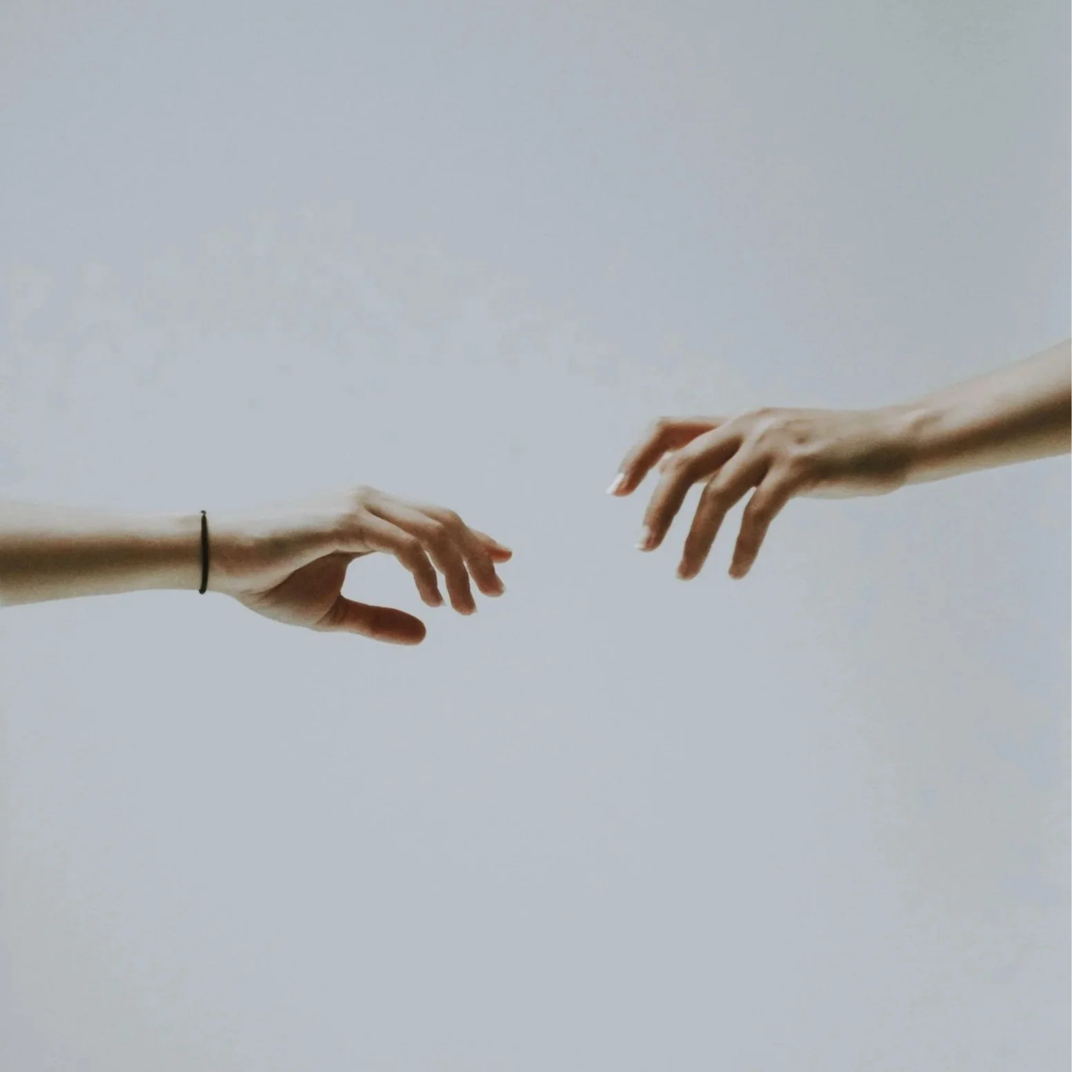 Two hands reaching towards each other, with only the hands and wrists visible, against a plain light background.