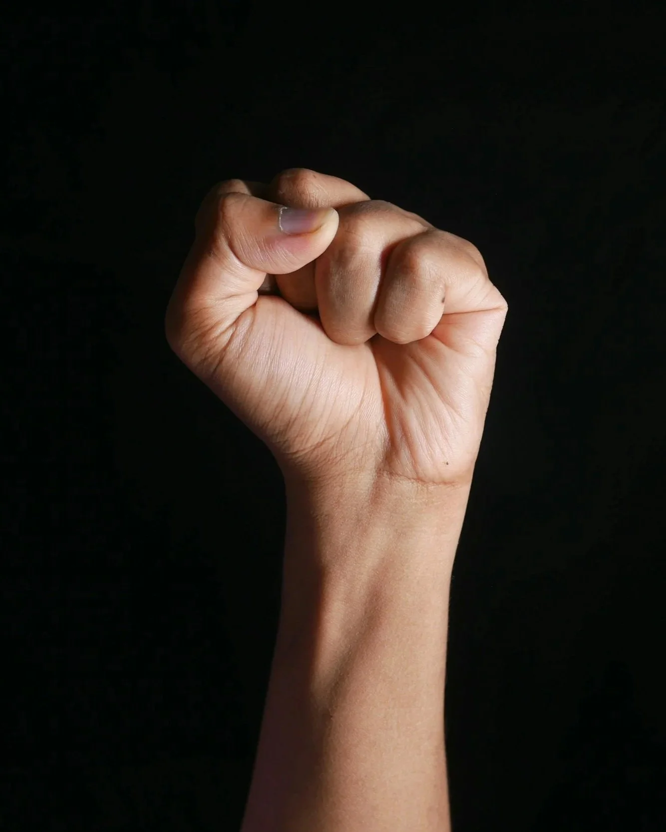 Close-up of a raised right hand with clenched fingers, against a dark background.