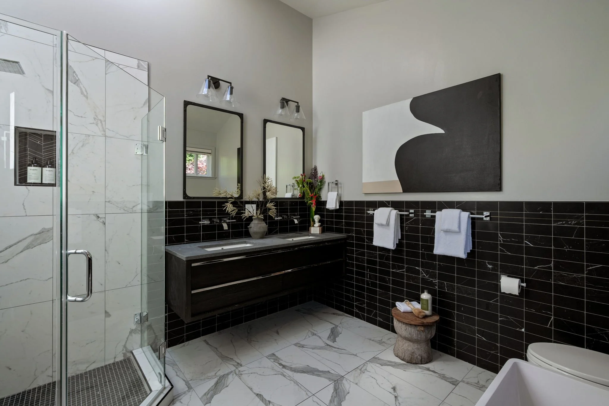 Modern bathroom with black and white marble tiles, a glass shower enclosure, a double vanity with mirrors, and various decorative plants and towels.