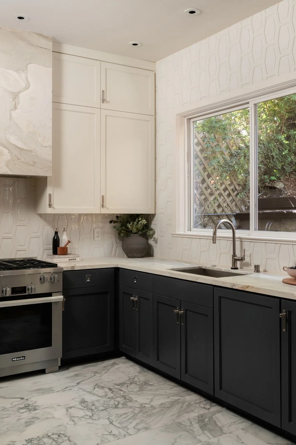 Kitchen with white and black cabinets, marble countertop, large window, and marble floor.
