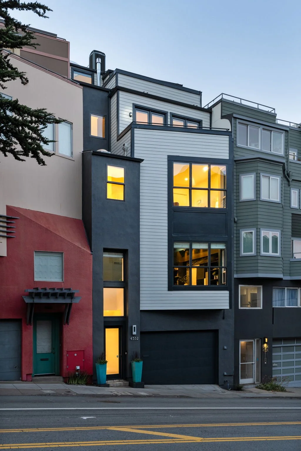 Modern multi-story residential building with colorful exterior walls and large windows illuminated from inside, situated on a city street.