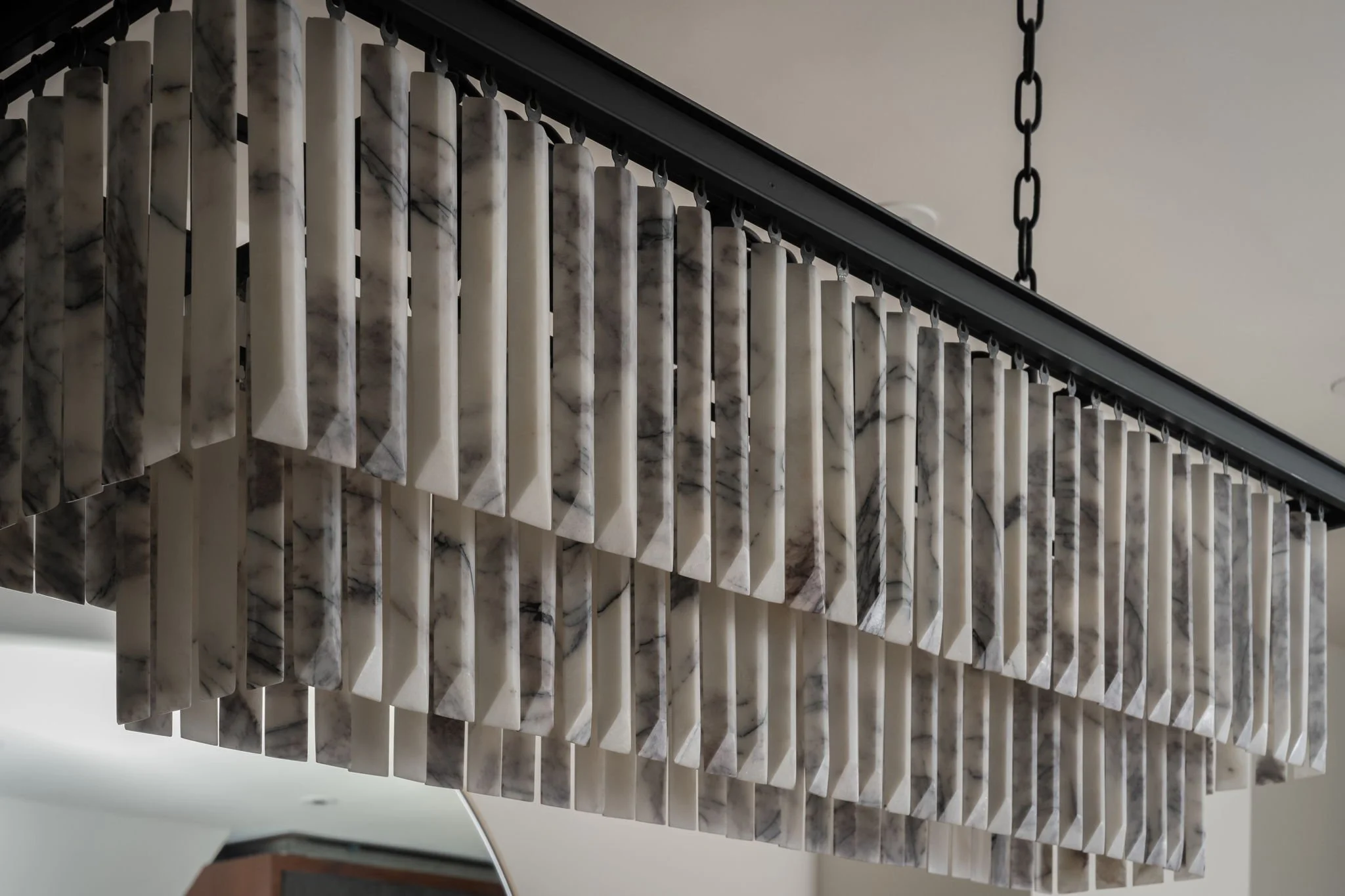 Close-up of a modern chandelier made of multiple rectangular marble tiles hanging from black chains.