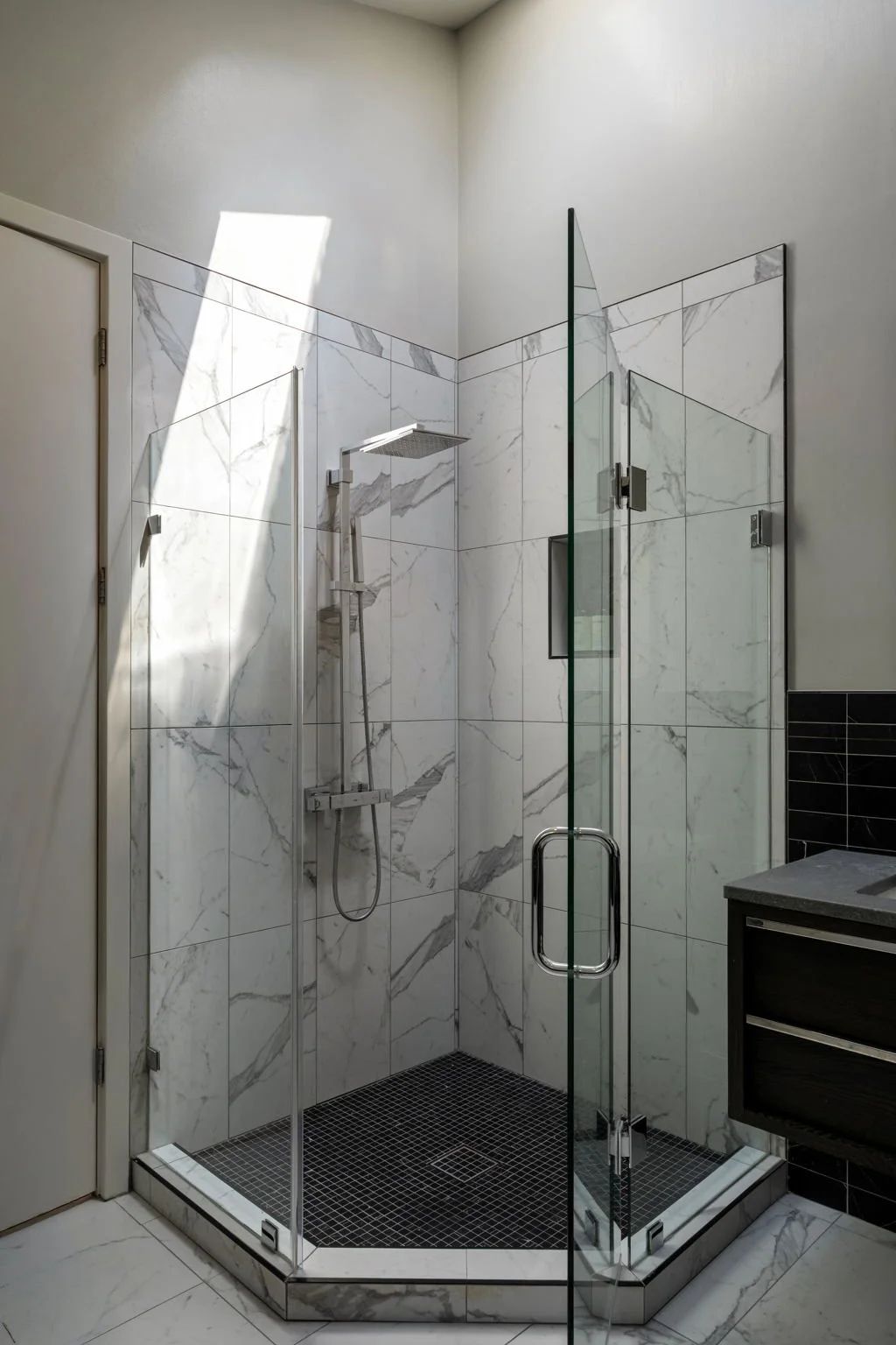 Modern shower with marble tiles, glass enclosure, rainfall showerhead, and black tile floor.