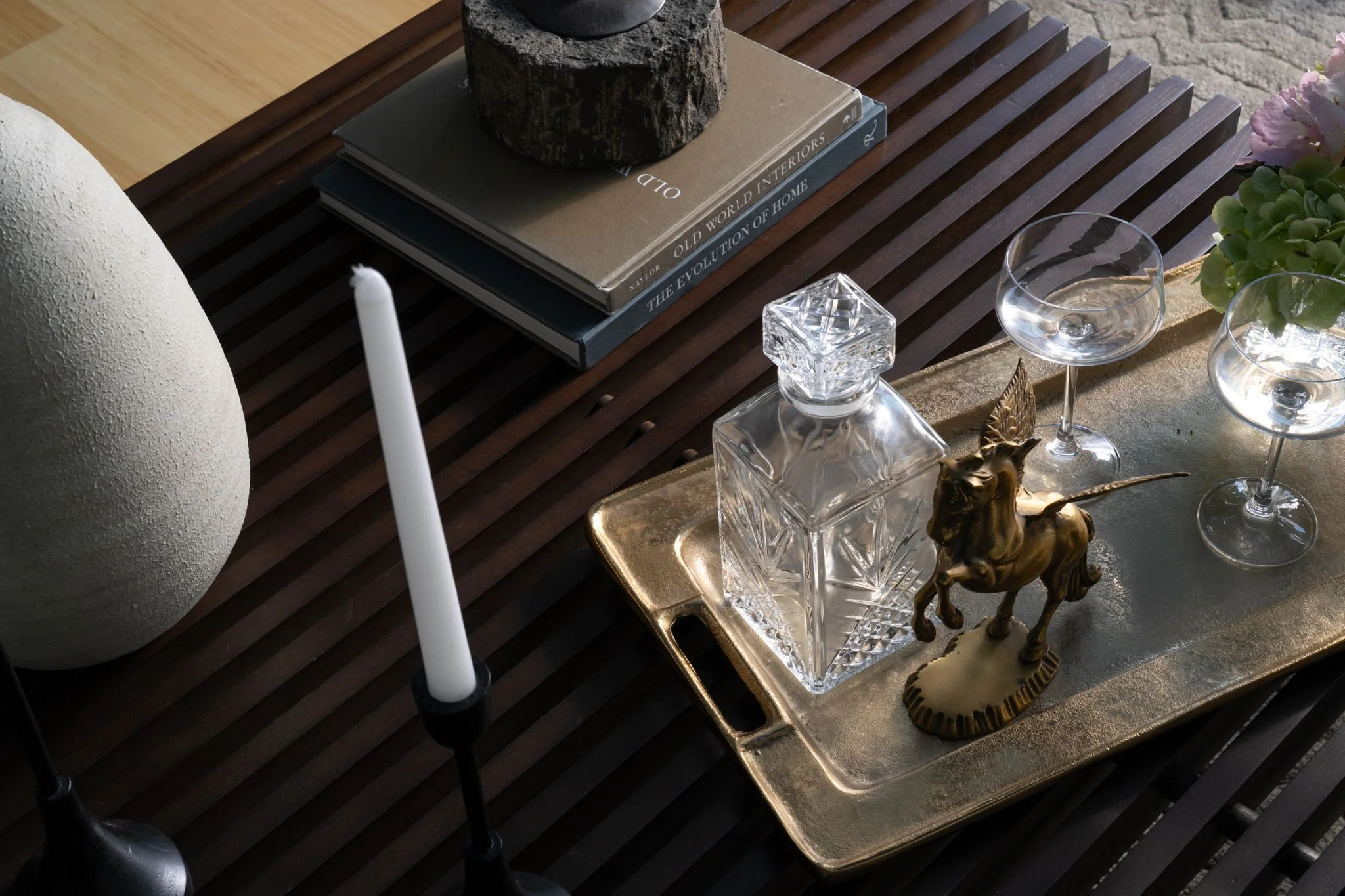 Decorative table arrangement with books, a candle, a glass sculpture, and a small golden horse figurine on a wooden slatted table.