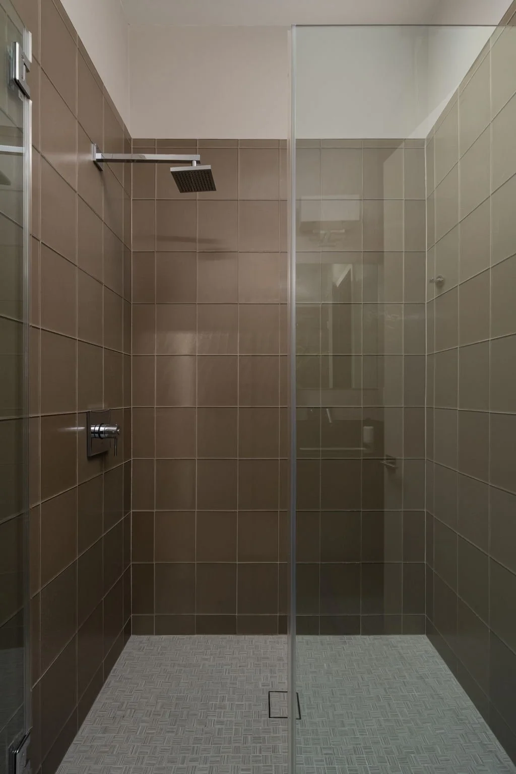 Empty shower area with brown tiled walls, a square overhead shower, and a glass partition.