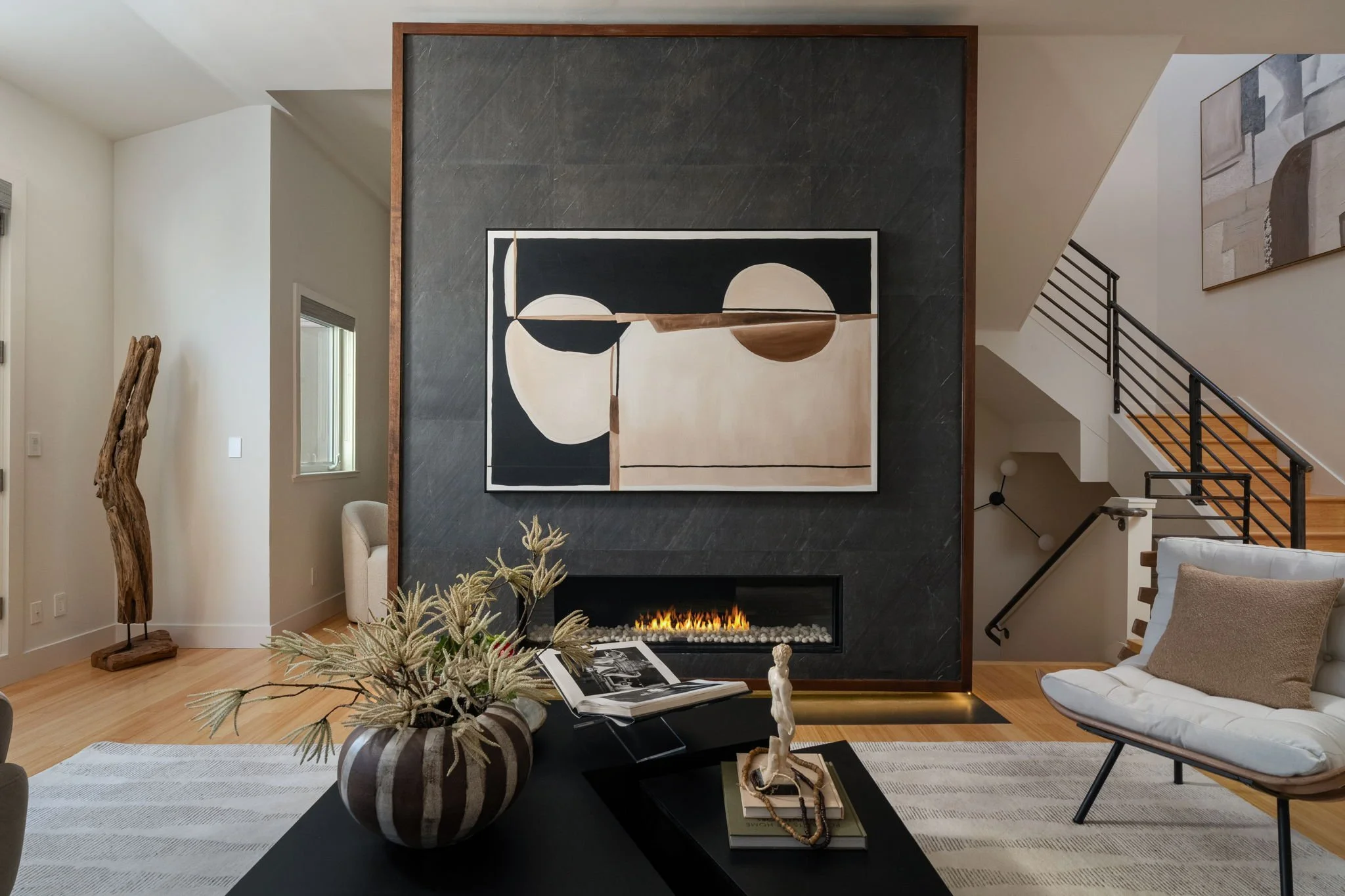 Modern living room with a black fireplace, abstract artwork, white walls, wooden flooring, and contemporary furniture.