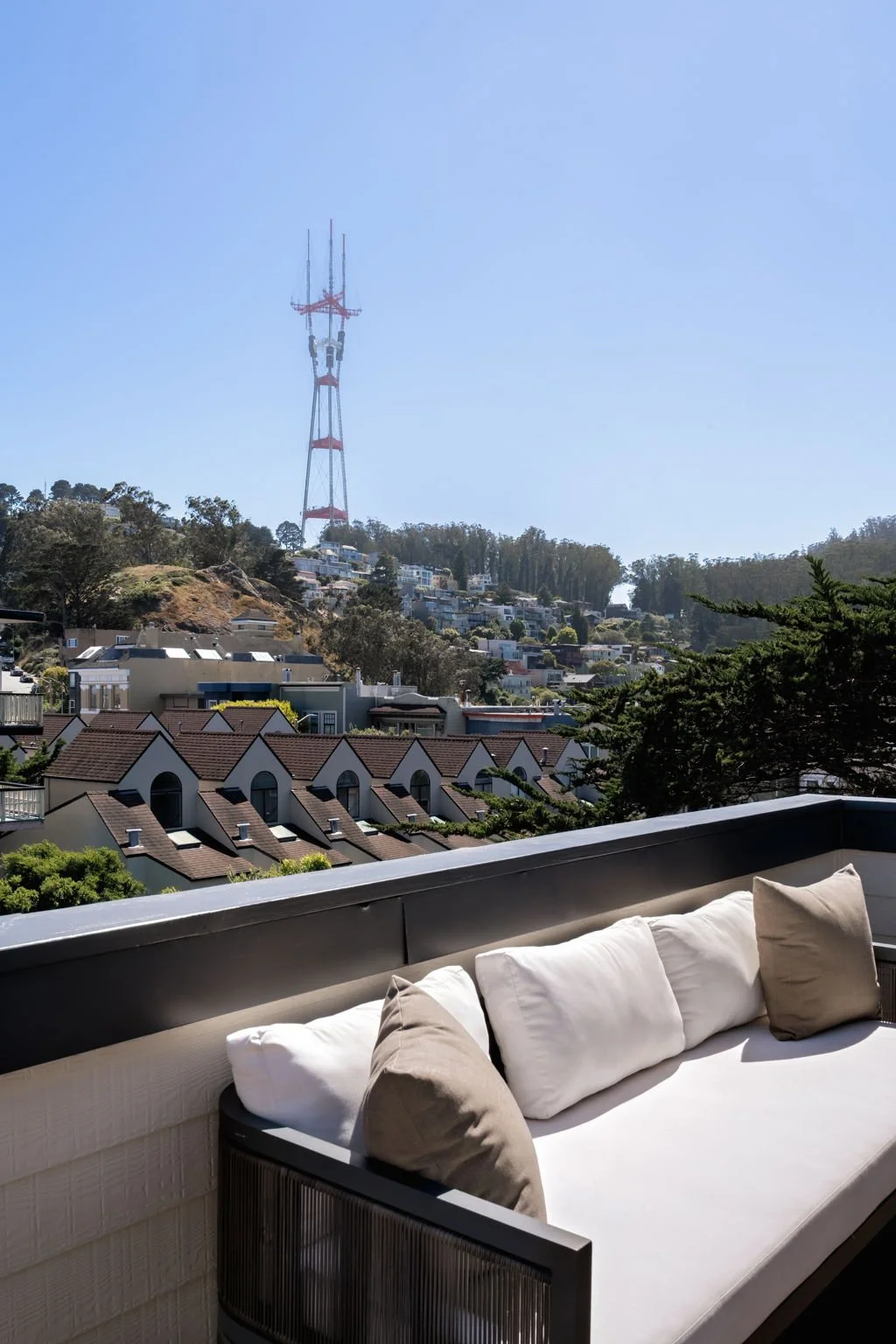 Balcony view of a hillside with residential houses and a large communication tower on top of the hill, under a clear blue sky.