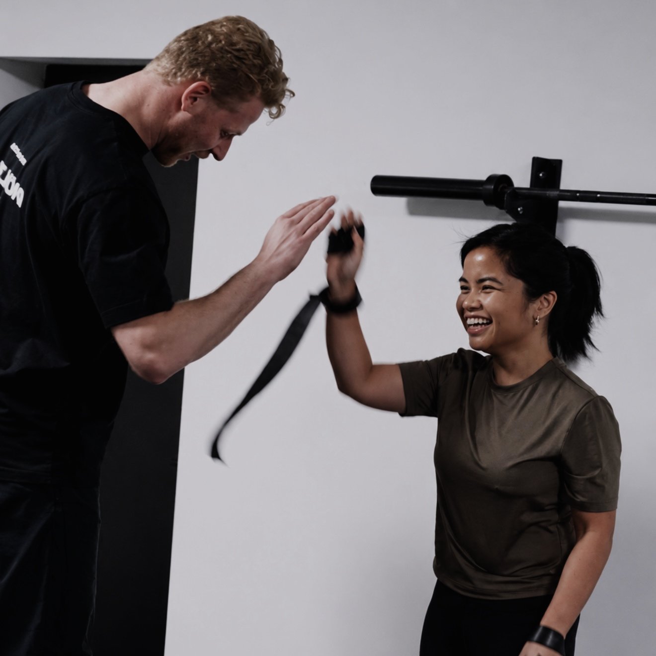 Two people smiling and high-fiving during a gym workout with suspension training straps.