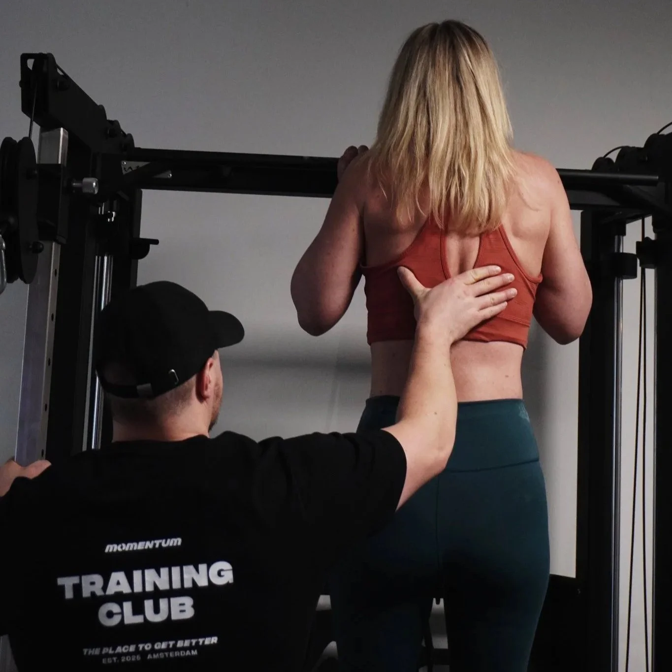 Personal trainer spots a woman performing a barbell squat in a gym.