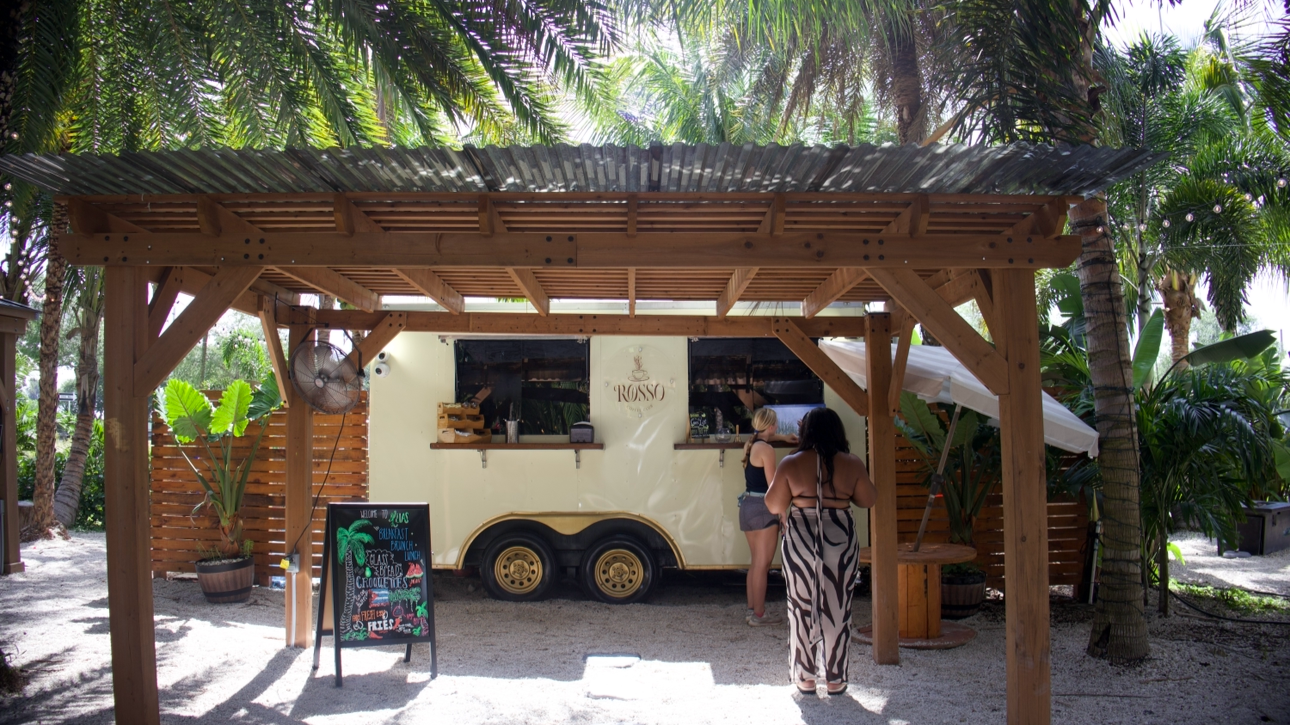 Outdoor hospitality venue with food truck, palm trees, and guest gathering area.