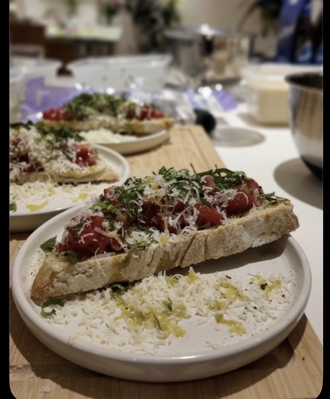 Close-up of a plate with a stuffed pizza slice topped with chopped tomatoes, herbs, and cheese, served on a bed of grated cheese with olive oil drizzle. Other similar plates are visible in the background.