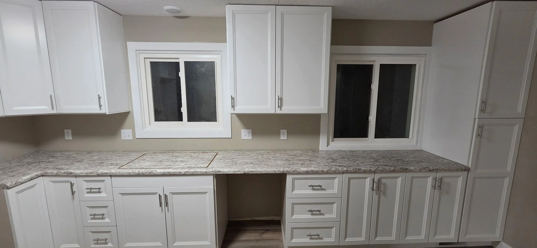 Kitchen cabinets with granite countertops and two windows with white frames.