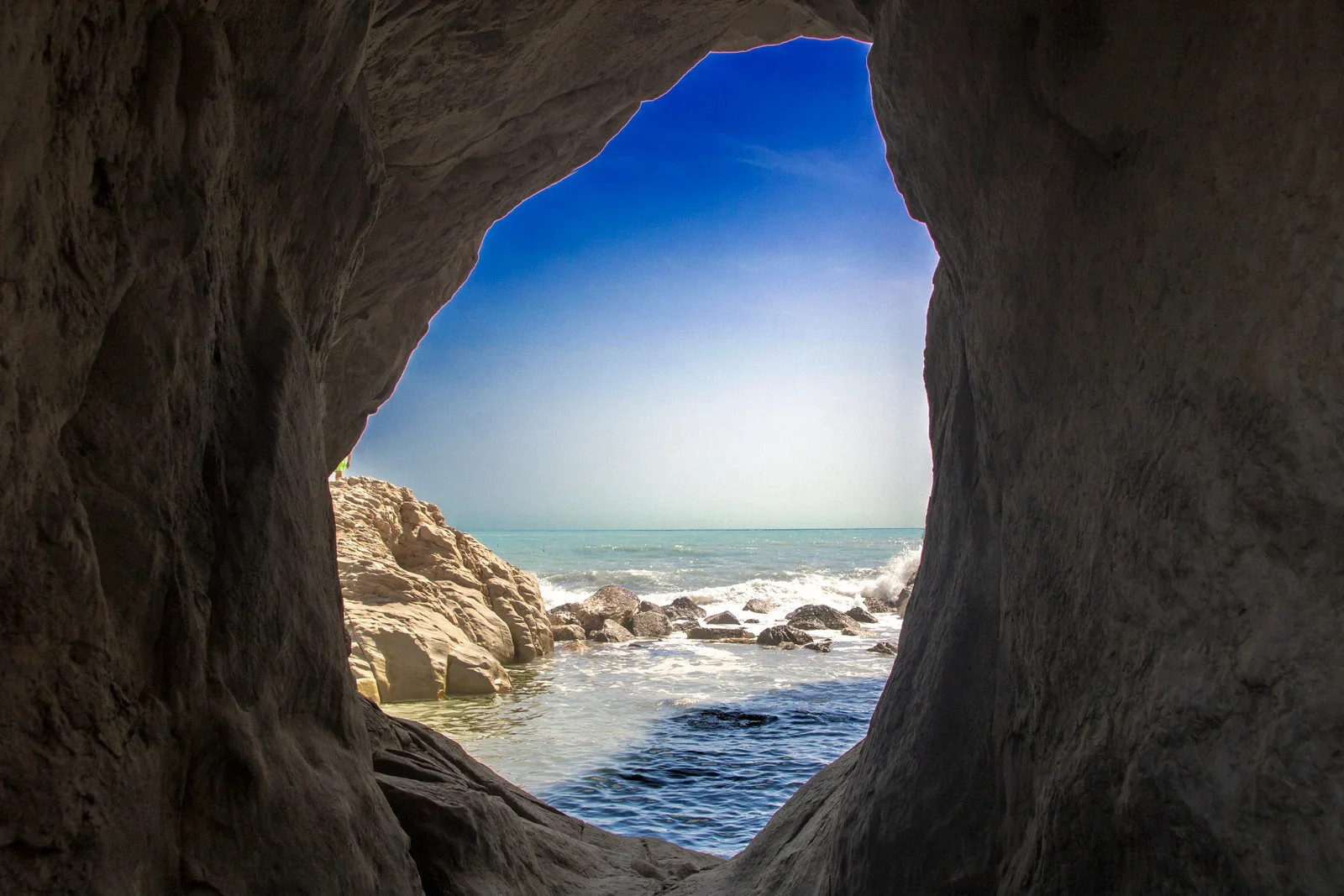 View of the ocean and beach through a rock opening or cave