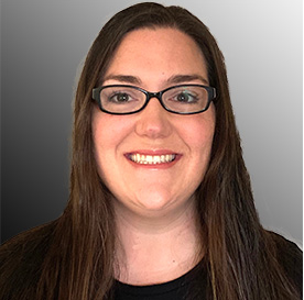 A woman with long brown hair, glasses, and a friendly smile, wearing a black top, against a gray background.