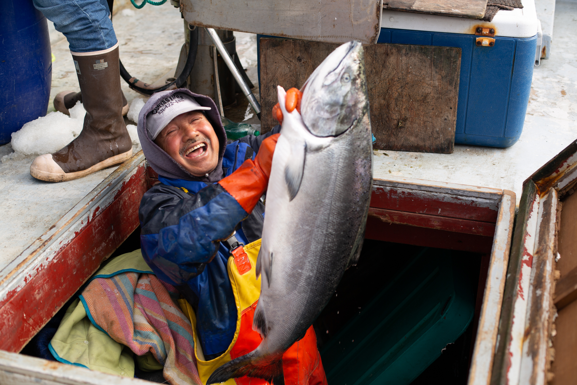 A man in rain gear holding a large fish on a boat.