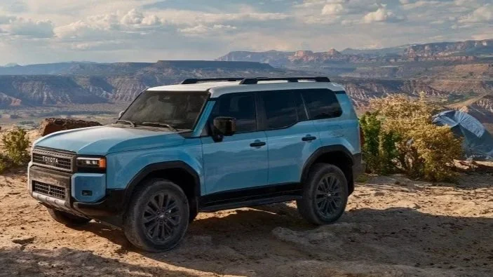 Blue SUV parked on desert landscape with canyon views and cloudy sky in the background.