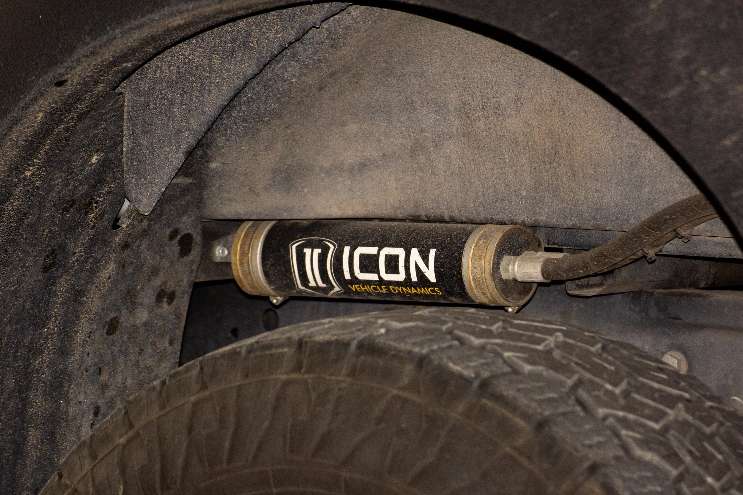 Close-up of a vehicle's suspension component labeled 'ICON Vehicle Dynamics,' with a dusty black wheel and tire nearby.