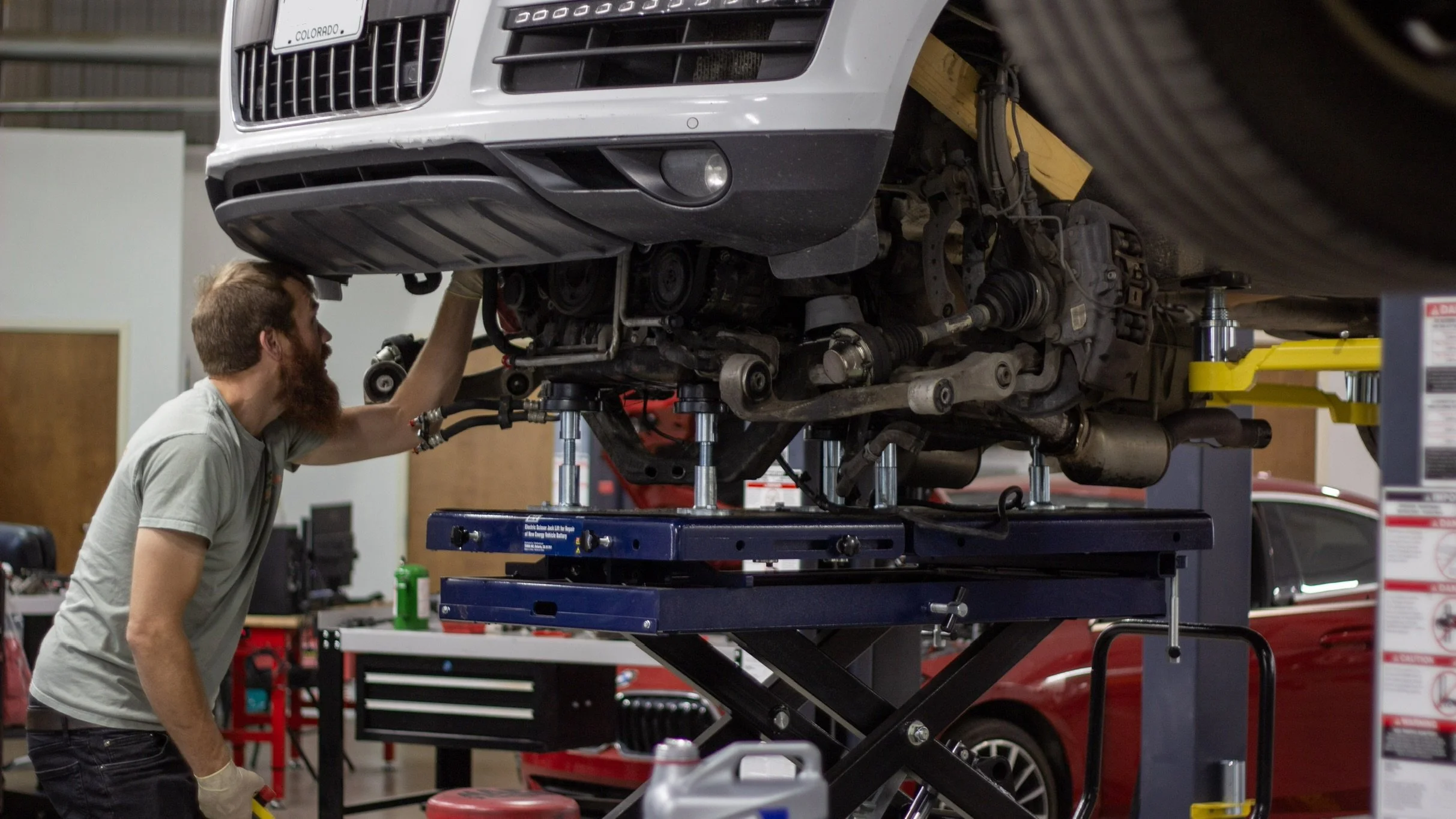 Tyler, owner,  working underneath a white Audi car that is lifted on a hydraulic lift in an automotive repair shop.