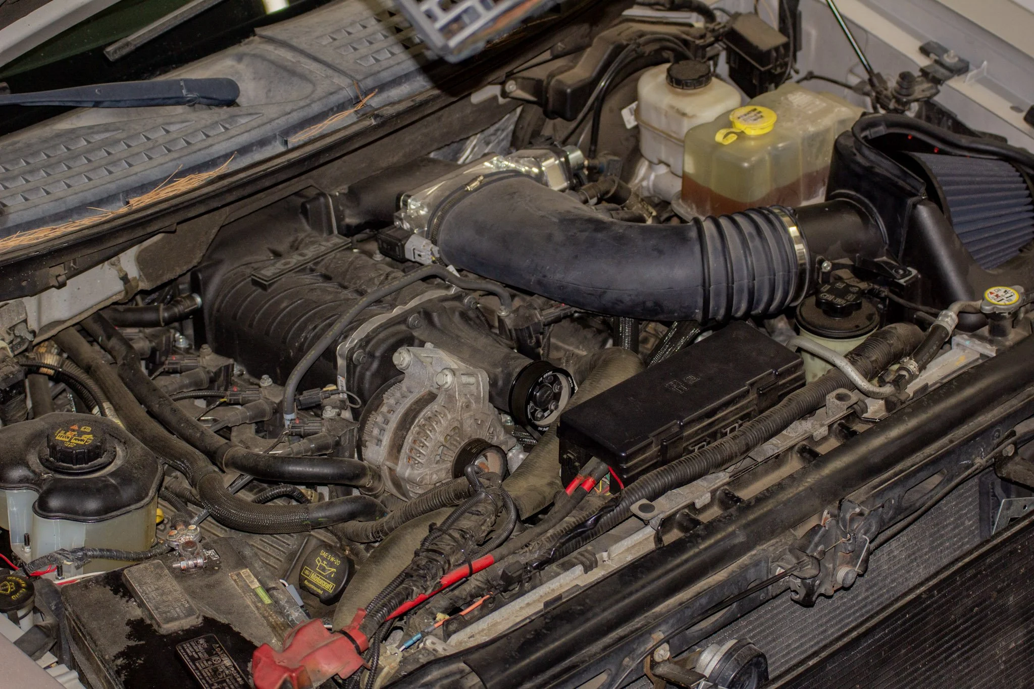 Close-up of a car engine bay showing various engine components, hoses, and fluid reservoirs.