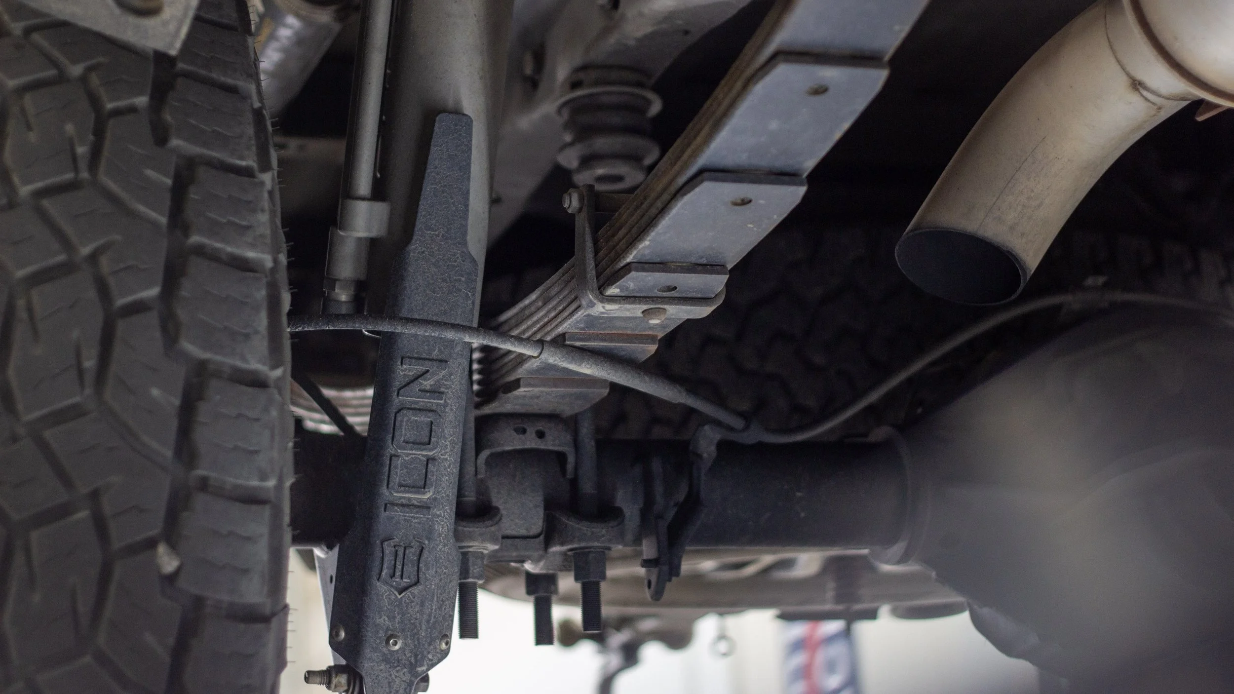Underneath view of a vehicle showing the suspension, exhaust pipe, and tire.