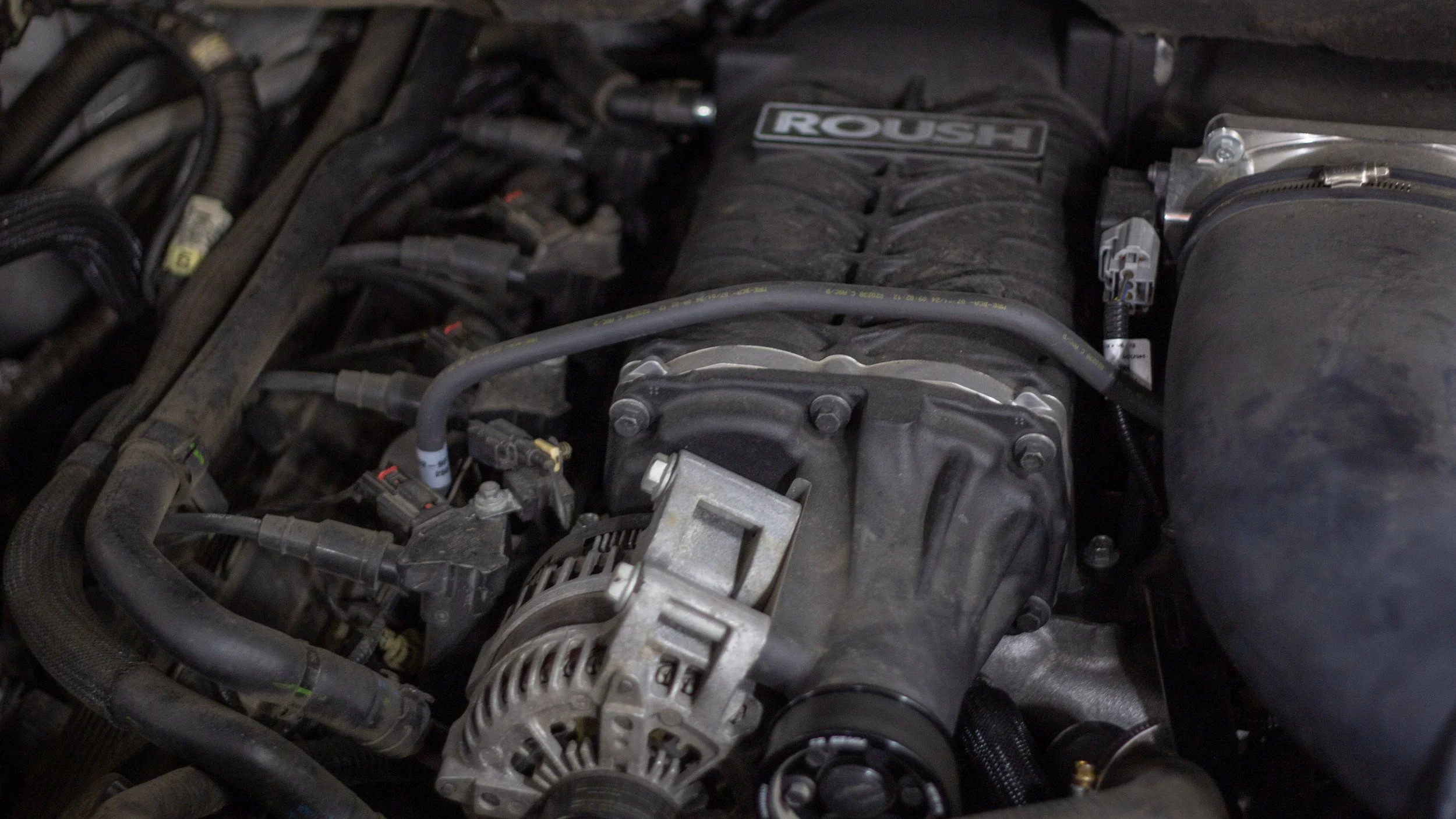 Close-up of a car engine with various hoses, wires, and metal components visible.