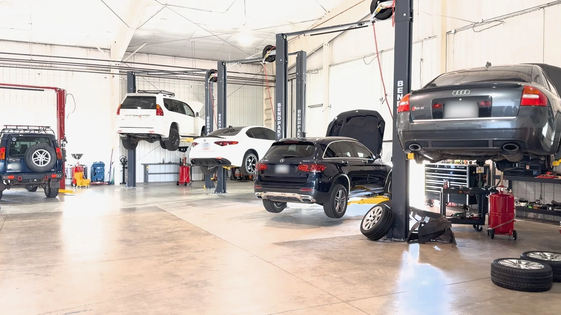 EuroSpring shop with multiple cars elevated on lifts. Various tools and equipment in the background. Audi, Mercedes, Alfa Romeo, Lexus, and Land Rover on the lifts.