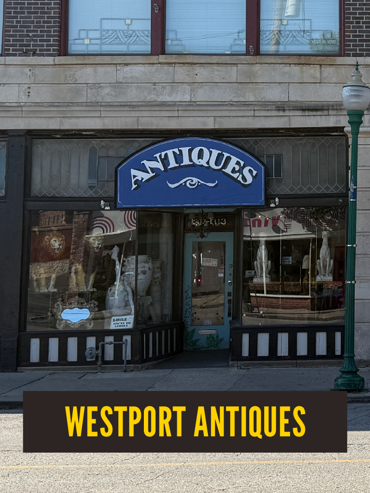 The storefront has a blue sign with white text that says "ANTIQUES." The shop's window displays various antique items, including sculptures and pottery. The bottom of the image has a black and yellow sign that says "WESTPORT ANTIQUES."  Westport East