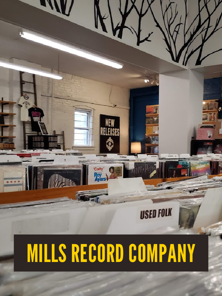 Inside a record store with vinyl records organized in bins, a sign indicates 'Used Folk', and a poster advertises 'New Releases'. The store has shelving, a ladder, and decorative elements on the ceiling. Mills Record Company. Broadway. Westport East.
