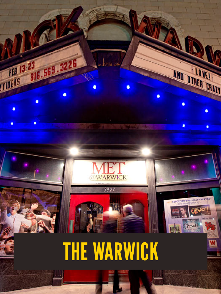 Marquee sign for the Warwick Theatre with blue lights and posters in the window, outside the building at night, with a black banner that reads 'The Warwick'.  Westport East.