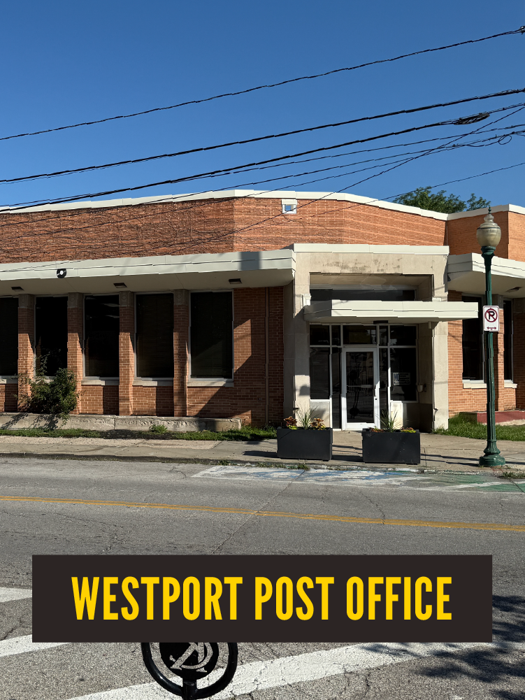 A brick building with large front windows and an entrance with glass doors, signifying the Westport Post Office, with a sidewalk, street, street lamp, and overhead power lines in front of it.  Westport East. USPS