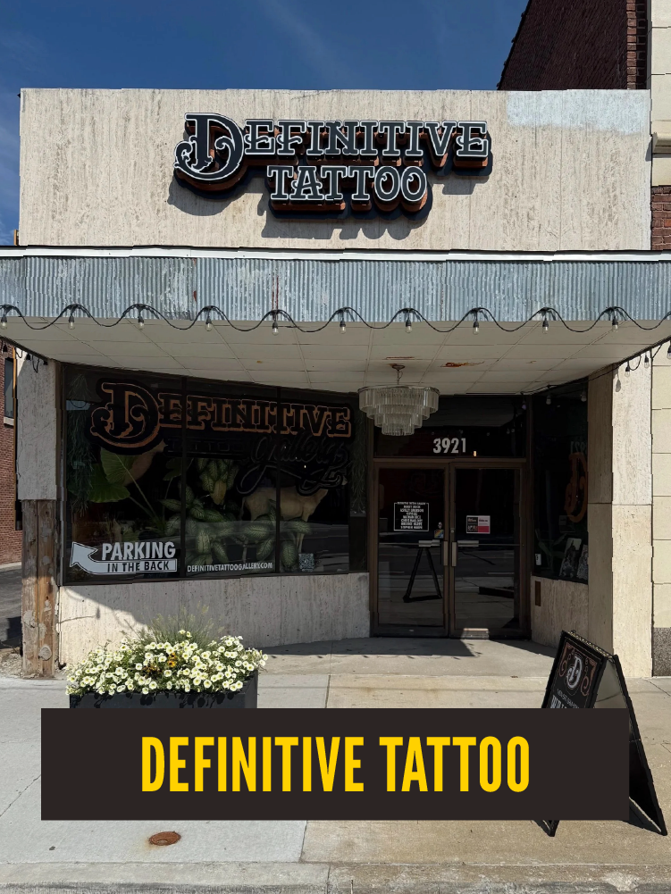  storefront for 'Definitive Tattoo' with a sign above the entrance, window advertisement, and a black sign on the sidewalk in front of the store.  Westport East.