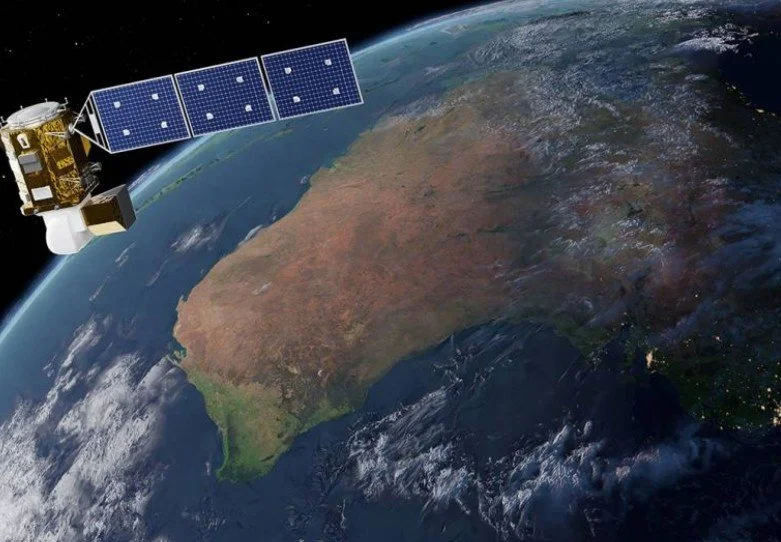 A satellite orbiting Earth shows the landmass of Australia with satellite solar panels extended in space.