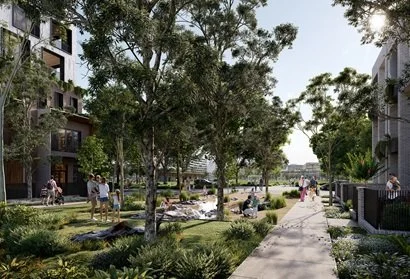 People walking and relaxing in a landscaped park with trees, grass, and a paved pathway.