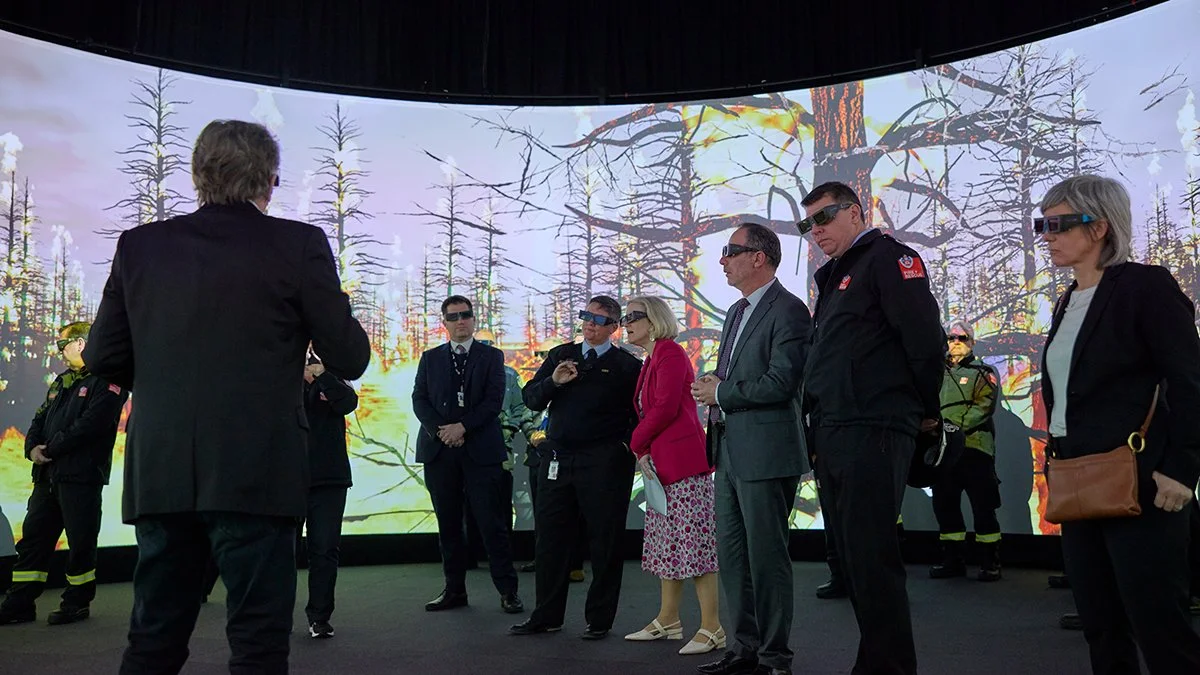 People observing a large digital display showing a forest fire, with some wearing 3D glasses.